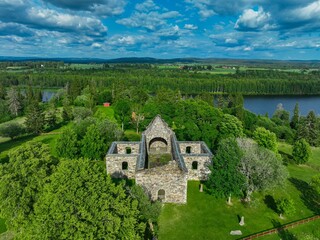 Fototapeta na wymiar Aerial view of a weathered old building ruins surrounded by lush green trees and a pond
