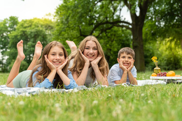 Portrait of happy three children lying in the park on a blanket on the grass. Two blond girls and...