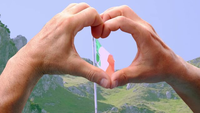 closeup of male hands in heart form against national flag of state of Italy on silk, beautiful mountains, concept of tourism, emigration, economy, politics, civil rights and freedoms, independence day
