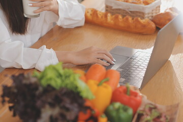 Portrait of pretty freelancer female working typing on laptop computer sitting at table smiling looking to screen in kitchen. Attractive redhead young woman remote working on laptop from home office.