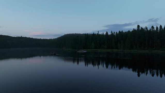 Aerial of a calm lake surrounded by dense calm forest during the early morning