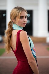 Vertical shot of a young blonde female in a red dress and a scarf posing