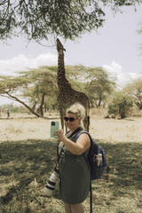 Lake Naivasha - tourist woman on a walking safari takes a selfie with a wild giraffe as it eats