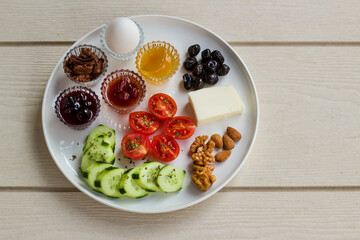 White breakfast plate with sliced cherry tomatoes, cucumber and boiled egg with copy space on wooden table.Top view