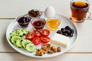 White breakfast plate with sliced cherry tomatoes, cucumber and boiled egg with tea cup on wooden table