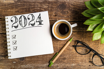 New year goals 2024 on desk. 2024 goals list with notebook, coffee cup, plant on wooden table. Resolutions, plan, goals, action, checklist, idea concept. New Year 2024 template, copy space - obrazy, fototapety, plakaty