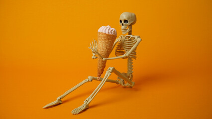 Sitting skeleton witn ice cream on a yellow background.              