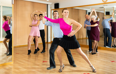 Fototapeta na wymiar Dynamic middle-aged pair engaging in ballroom dance in dance studio. Pairs training ballroom dance in hall