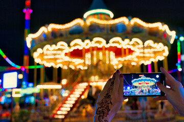 Fototapeta na wymiar Young girl takes a photo with her mobile phone in the evening. Global Village, Dubai, UAE.
