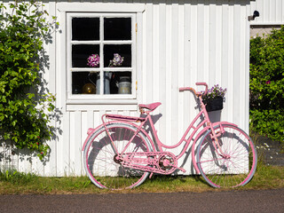 Fototapeta na wymiar Vrango, Sweden - May 31, 2023: A pink bicycle leaning against a white wooden Swedish house