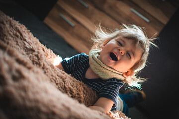 Kind tobt auf braunem Kuschelkissen und lacht herzhaft