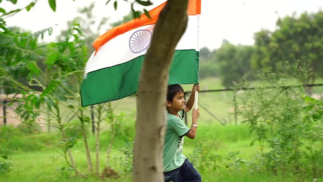 Cute little Indian kids holding, waving or running with Tricolour with greenery in the background, celebrating Independence or Republic day