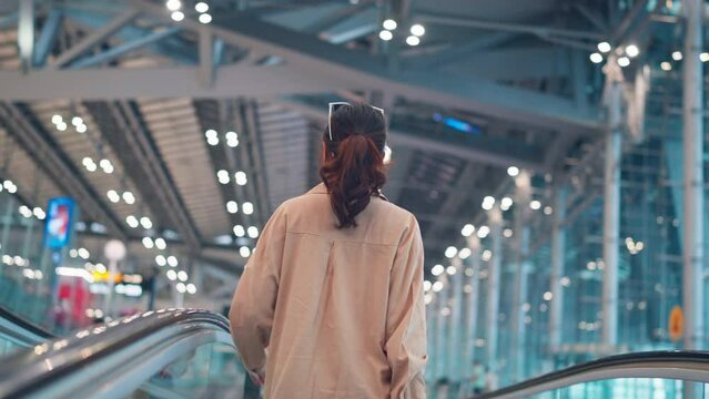 Asian tourist woman traveller with simple suitcase stand on moving walkway in airport terminal, Tourist journey trip concept.