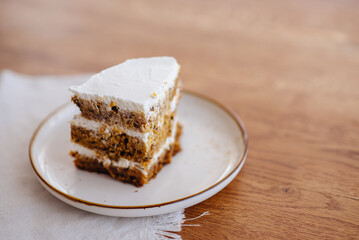 a piece of carrot cake with white cream on a plate on a wooden table