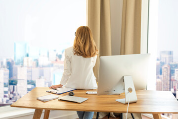 Rear view shot of a businesswoman standing at office desk and looking out over the city
