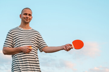 man holding ping pong paddle table tennis paddle on sky background. Mock-up copy space. Poster...