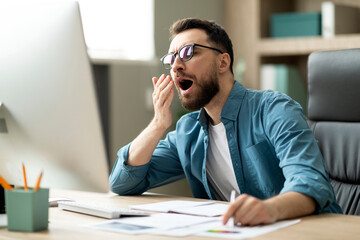 Portrait Of Sleepy Young Businessman Yawning At Workplace In Office - obrazy, fototapety, plakaty