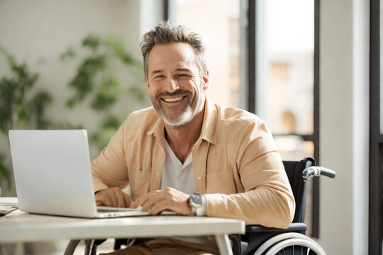 Hombre De Mediana Edad Feliz Sonriente Caucásico Sentado En Sillas De Ruedas En Un Escritorio Con Una Laptop, En Sala Con Buena Iluminacion, Ambiente Minimalista
