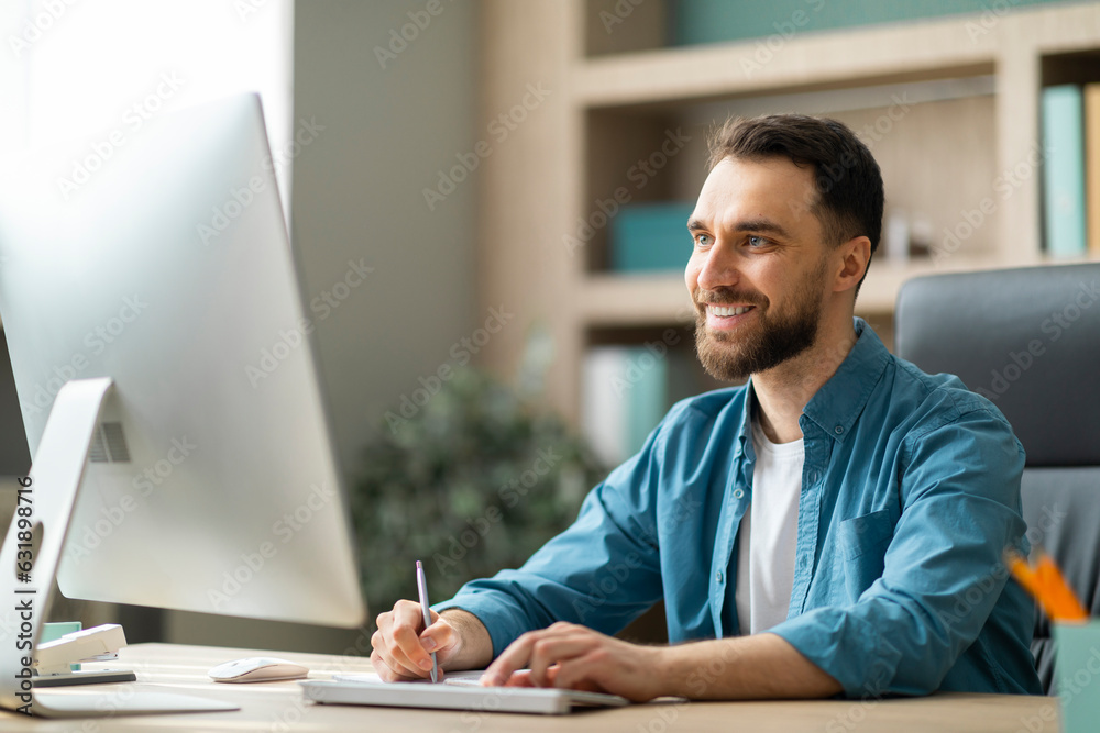 Aufkleber Young Smiling Businessman Taking Notes While Working On Computer In Office