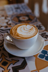 Cappuccino in a large white mug on a table with tiles. Coffee break at work