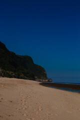 A large beach with a mountain and blue sky in the background. Scenic landscape concept