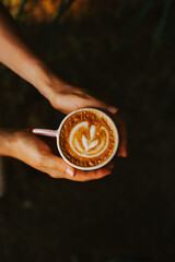 Women's hands holding delicious cappuccino coffee on a dark background. Creative and minimalistic concept of coffee with milk. with beautiful latte art