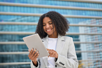 Happy young African American business woman holding digital tablet standing in city street, smiling busy sales professional ethnic lady corporate leader executive working outside office.