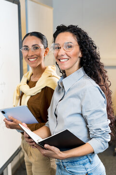 Vertical photo of two beautiful mixed race female students near blackboard with tablet and note book. Businesswoman smiling and looking at camera ready to plan start of school year. Learning concept
