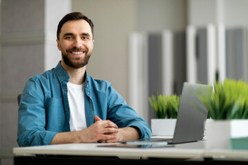 Fototapeta na wymiar Portrait of freelancer man sitting at desk with laptop computer at office
