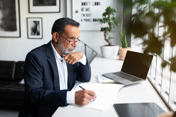 Pensive serious caucasian old businessman in suit with contract make notes, look at computer with empty screen