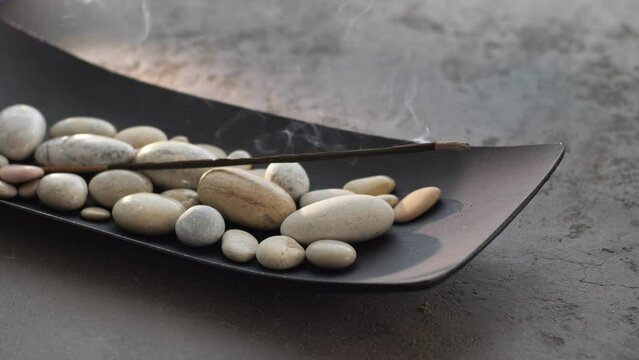 Burning incense aroma stick with smoke, fixed on pebble stones 