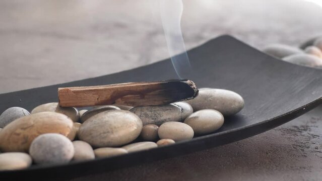 Burning Palo Santo stick with smoke on pebble stones 