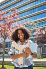 Happy smiling African American girl student standing outside university looking at camera outdoors,...