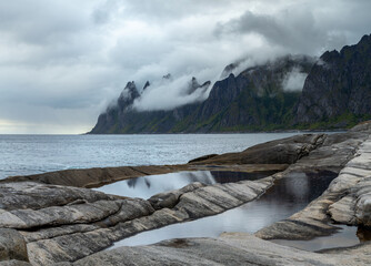 Rocky shoreline with mountains and cloudy sky