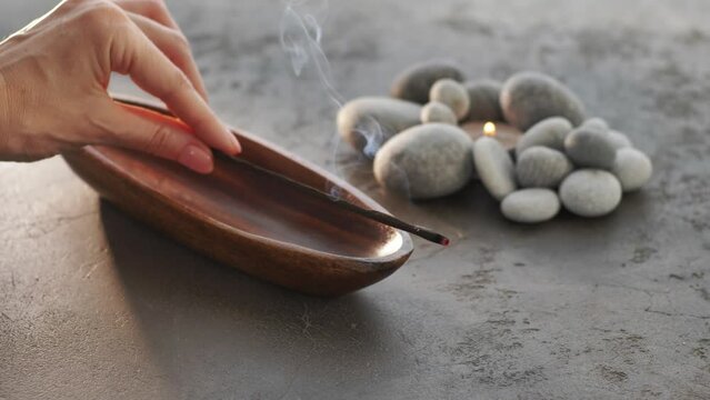 Burning incense aroma stick with smoke on wooden bowl, pebble stones on background