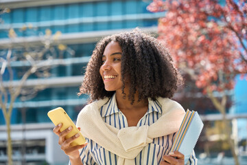 Smiling happy cute African teen girl student holding cellphone looking away with smartphone...