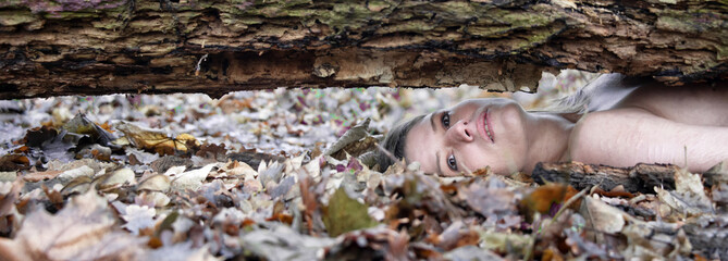 wide banner panorama portrait of sexy nude natural woman lying under fallen tree trunk, log in...