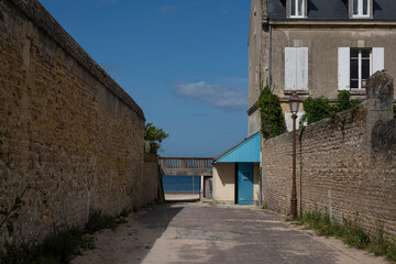 Fototapeta na wymiar Saint-Aubin-Sur-Mer, France - 07 19 2023: View of a narrow passageway with stone houses joining the jetty and the beach.