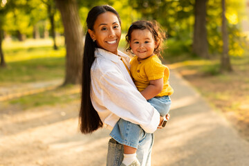 Loving Asian Mom Embracing and Holding Adorable Baby Daughter Outdoors