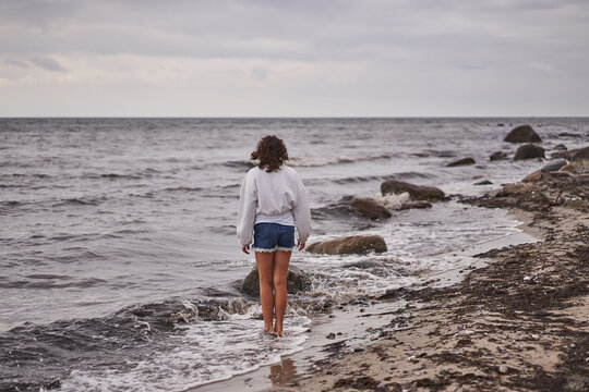 Teenage girl walking alone on the sand beach of North sea in Denmark during her summer holidays or vacation and watching horizon. Picture is taken during cloudy and windy summer scandinavian evening.