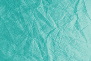 Wrinkled, crumpled turquoise fabric texture background. Wrinkled and creased abstract backdrop of spunbond textile, wallpaper with copy space, top view.