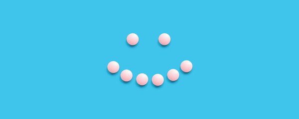 Smiling face lined with pink pills on a blue background, top view. Health care, medical pills and nutritional supplements. Pharmaceuticals