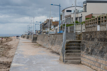 Fototapeta premium Saint-Aubin-Sur-Mer, France - 07 19 2023: View of a cloudy rainy sky, the seawall, staircases, houses and people above the sea from the jetty.