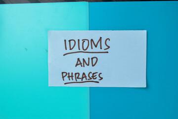 Concept of Idioms and Phrases write on sticky notes isolated on Wooden Table.