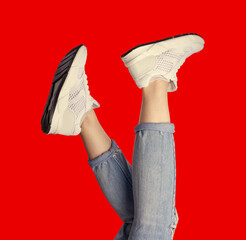 Female legs wearing trendy white sneakers and jeans isolated on a bright red background. Creative...