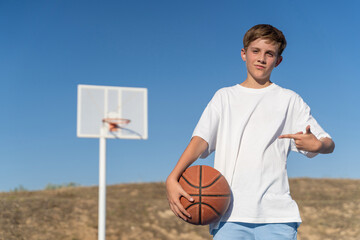 Young boy posing with a basketball ball while standing outdoors at a sports court. Sports concept.