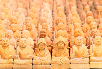 Background full of tiny wooden sculptures depicting buddhist monks meditating and surrounding the japanese Goddess of Mercy white-robed Byakue Kannon bodhisattva holding in their hand a toothpick.