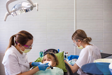 Dentist and assistant doing teeth little girl 5-6 year old in clinic. Dentist doctor having treating teeth treats at dental office kid girl. Concept of medical children dentistry. Copy ad text space
