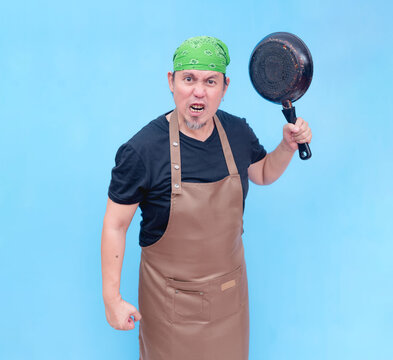 A furious and hostile middle-aged barista raising a frying pan threateningly. Isolated on a blue background.