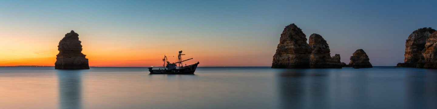Coastal dream - Fishing boat anchors between two beautiful rocks at sunrise in Algarve Portugal